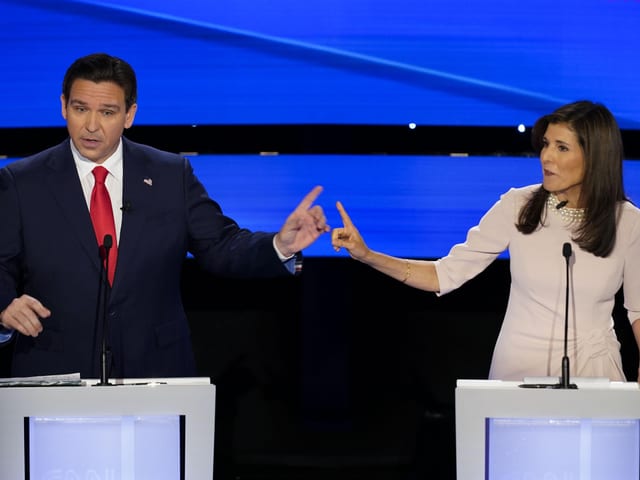 DeSantis und Haley stehen je an einem Rednerpult. Bei heben einen Zeigefinger. Sie diskutieren.