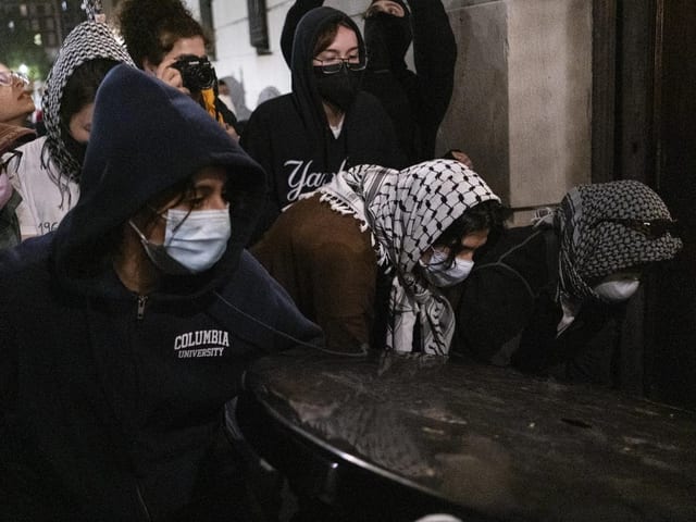 Menschen in Kapuzen und Masken bei einer nächtlichen Versammlung auf der Strasse.