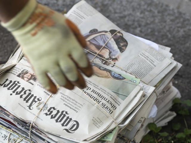 Hand in Handschuh greift nach einem Bündel Zeitungen