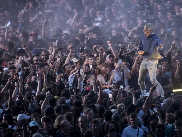 Rapper auf Bühne, er singt vor grosser Menschenmasse.