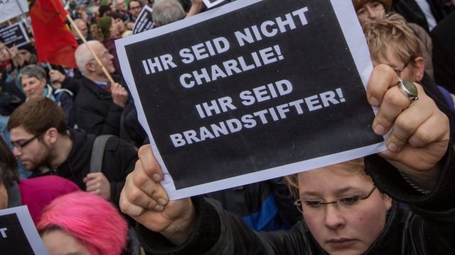 Eine Demonstrantin hält ein Schild hoch, auf dem in weisser Schrift auf schwarzem Grund «Ihr seid nicht Charlie! Ihr seid Brandstifter!» steht