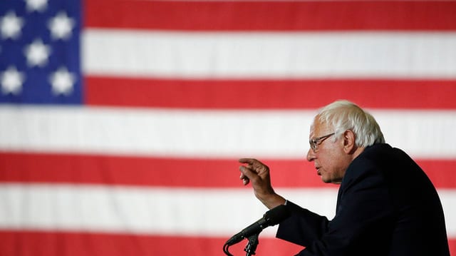 Bernie Sanders spricht vor seinen Anhängern und einer riesigen USA-Flagge.