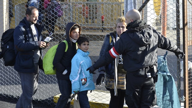 Flüchtlinge werden von einem österreichischen Grenzbeamten an einem Zaun weitergewiesen.