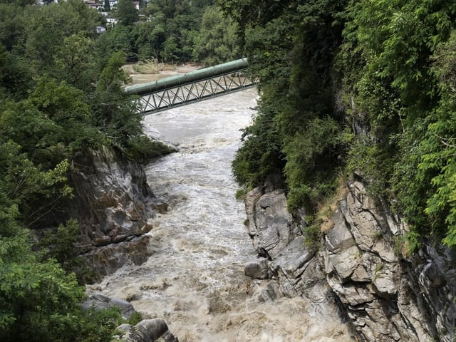 Fluss zwischen felsigen Ufern mit grünem Pipelinekorridor im Hintergrund.