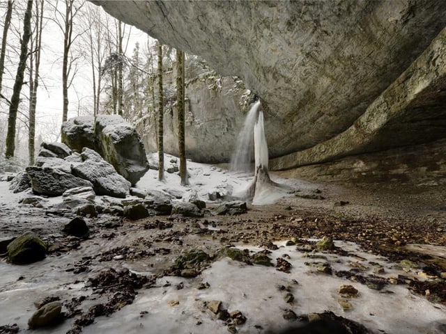 Eingefrorener Wasserfall in verschneitem Wald.