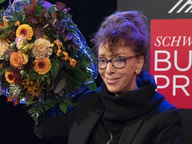 Frau mit lockigem Haar, Brille und Blumenstrauss.