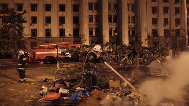 Ein Feuerwehrmann löscht Feuer vor einem Gebäude