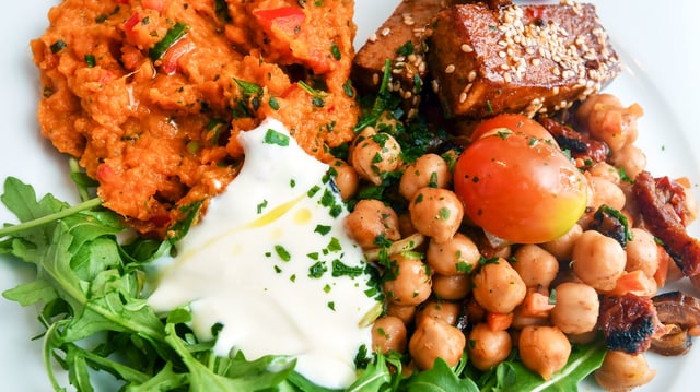 Ein Teller mit vegetarischen Zutaten wie zum Beispiel Tofu, Kichererbsen und Rucola. 