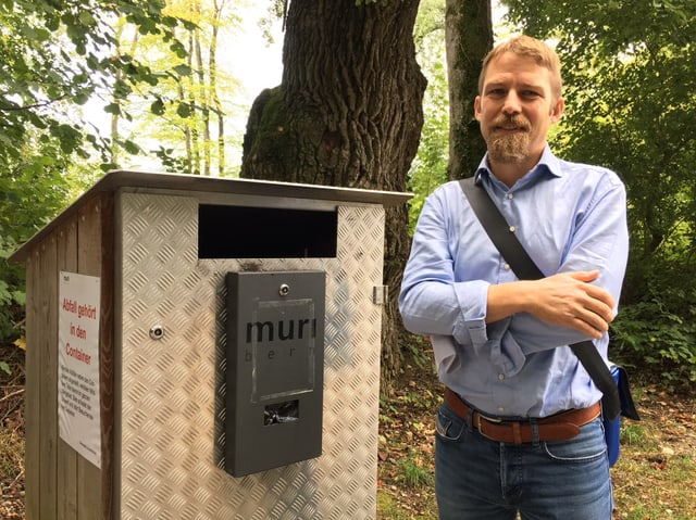 Mann steht neben Abfallcontainer im Wald.