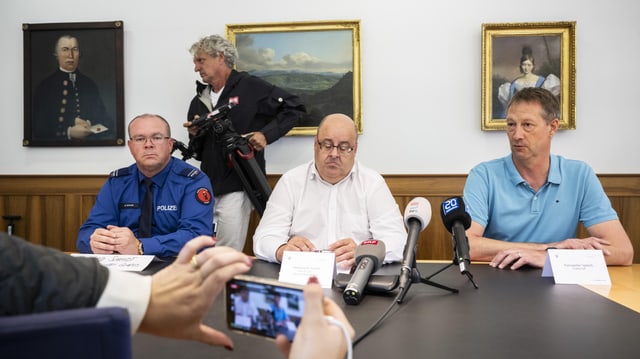 Drei Männer auf Podium an Pressekonferenz