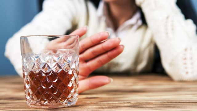 Auf dem Bild ist eine Frau zu sehen, die ein Glas Alkohol ablehnt.