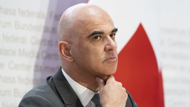 Alain Berset vor weiss-roter Wand, kritisch-nachdenklich