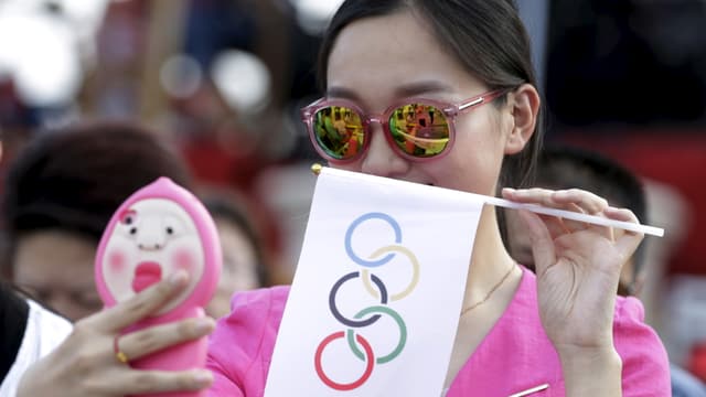 Eine Chinesin mit Sonnebrille und einem Wimpel mit Olympischen Ringen macht ein Selfie.