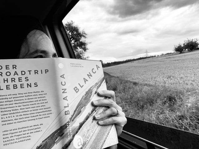 Annette König hält das Buch  «Blanca» von Mercedes Lauenstein in den Händen und schaut aus einem Autofenster hinaus