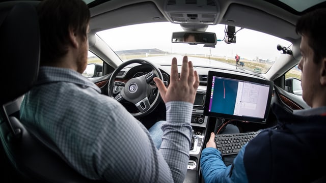 Zwei Männer in einem Auto, die Hände sind nicht am Lenkrad. Das Auto fährt autonom.