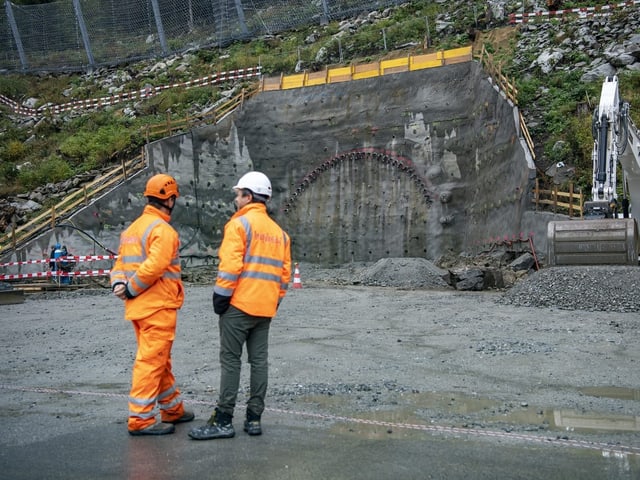 Bauarbeiter stehen in der Nähe des angefangenen Tunnelportals.