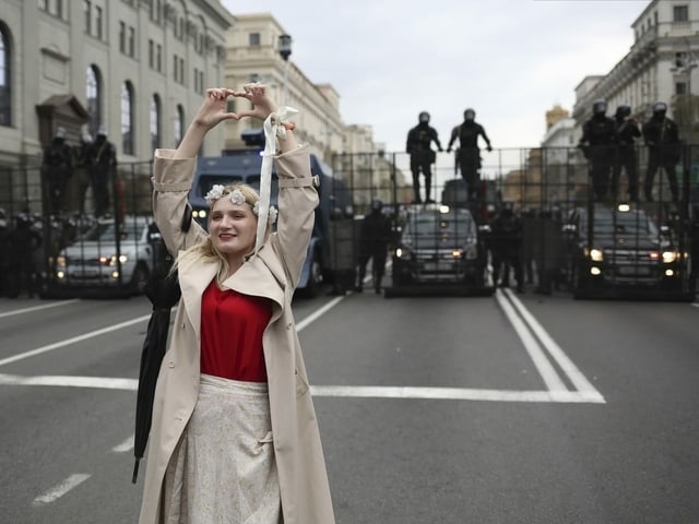 A woman makes a heart with her hands and stands in front of the security forces.