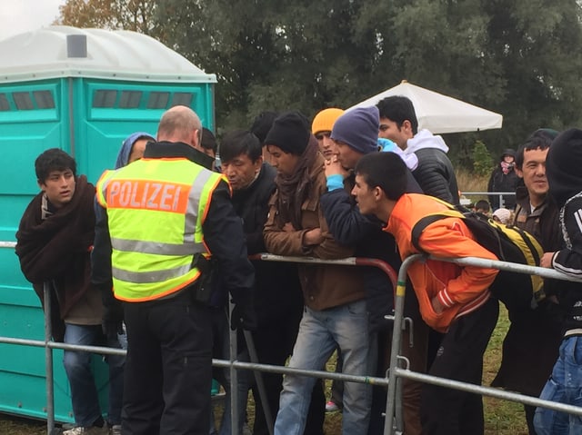 Junge Männer stehen um einen Mann mit Jacke «Polizei», im Hintergrund eine mobile Toilette.