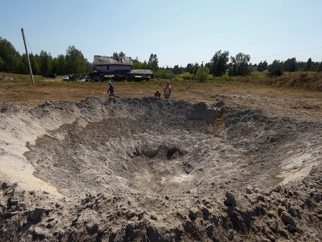 Grosser Krater im Boden vor einem abgelegenen Haus.