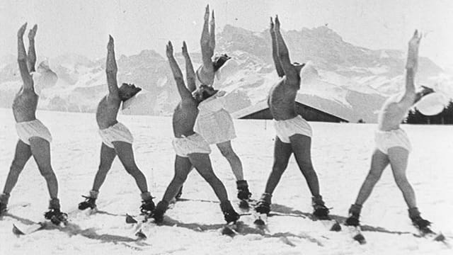 Menschen in Unterhose und mit Sonnenhut turnen auf