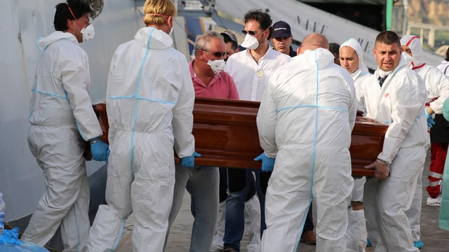 Männer, die einen Holzsarg aus einem Schiff ausladen