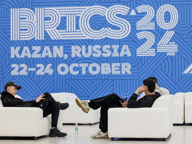 Personen auf weissen Sofas vor BRICS 2024 Plakat.