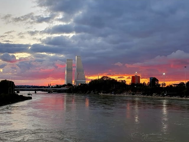 Sonnenuntergang über Fluss mit Wolkenkratzern im Hintergrund.