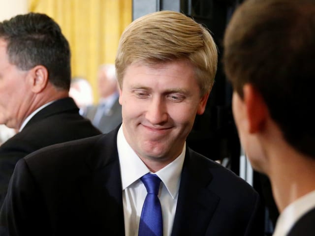 Nick Ayers im Gespräch, er trägt einen dunklen Anzug, ein weisses Hemd mit blauer Krawatte.