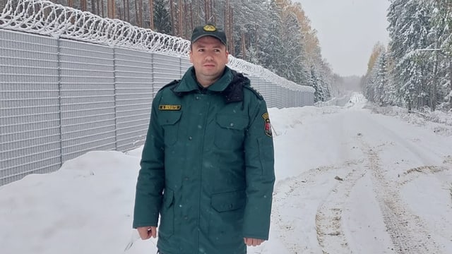 Mann in Uniform vor Grenzzaun. Es ist alles verschneit.