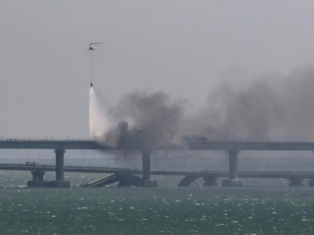 Ein Helikopter fliegt über der Brücke und lässt eine Wasserladung fallen. 