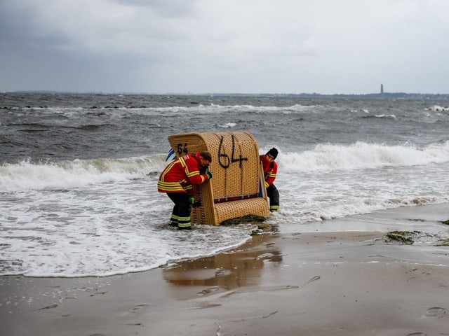 Zwei Männer verhindern, das ein Strandkorb von den Wellen mitgerissen wird.