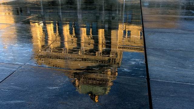 Spiegelung des Bundeshauses in einer Wasserlache.