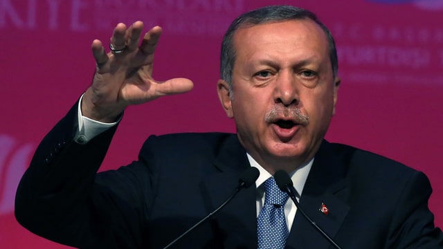 Erdogan spricht in zwei Mikrofone, die rechte Hand mit gespreizten Fingern erhoben.