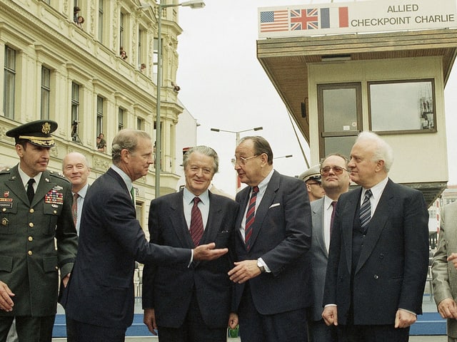 Genscher mit seinen Amtskollegen James Baker (USA) und dem Franzosen Roland Dumas (links) sowie Eduard Schewardnadse (rechts), im HIntergrund das Wachhaus, das von einem Kran in die Höhe gehoben wird.