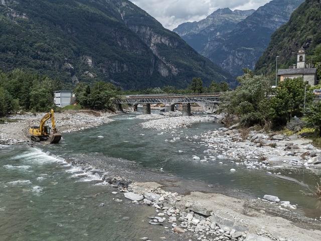 Ein gelber Bagger am Ufer der kiesgefüllten Maggia bei Cevio.