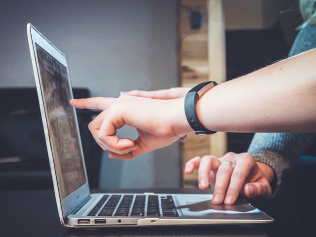 Laptop von der Seite eine Hand zeigt auf den Bildschirm