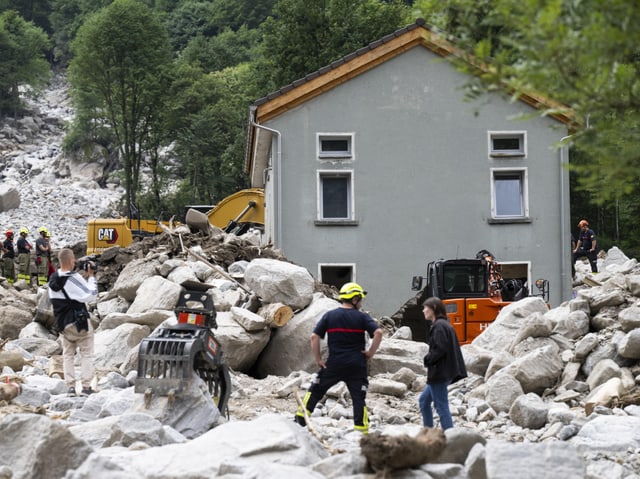 Rettungskräfte bei einem Erdrutsch vor einem beschädigten Haus.