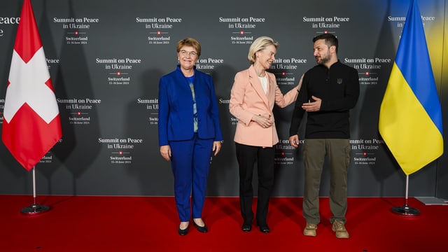 Drei Personen stehen auf rotem Teppich, Schweizer und ukrainische Flagge im Hintergrund.