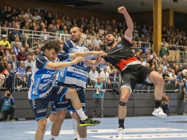 Handballspieler im Zweikampf während eines Spiels in einer Sporthalle.