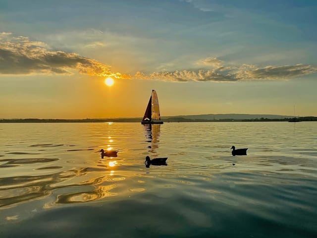 See mit Segelschiff bei Sonnenuntergang