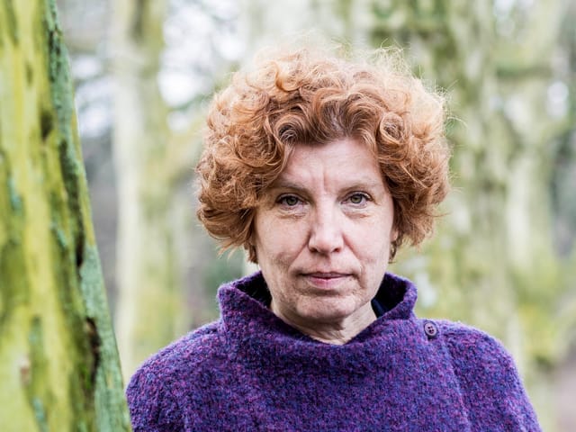 Frau mit lockigem, rotem Haar in lila Pullover im Wald.