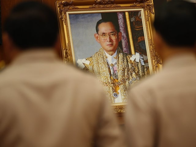 Silhouette von zwei Männern, die vor einem Foto von König Bhumibol stehen.