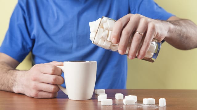 Mann schüttet ganz viel Zucker in den Kaffee.