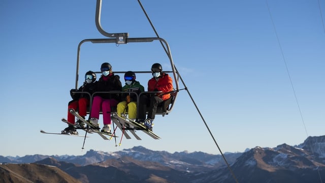 Maskentragende Skifahrer auf Sessellift.