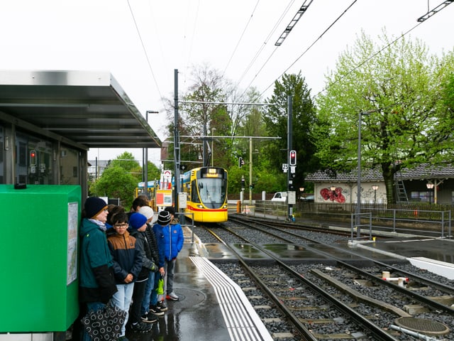 Kinder warten an der Haltestelle aufs Tram.