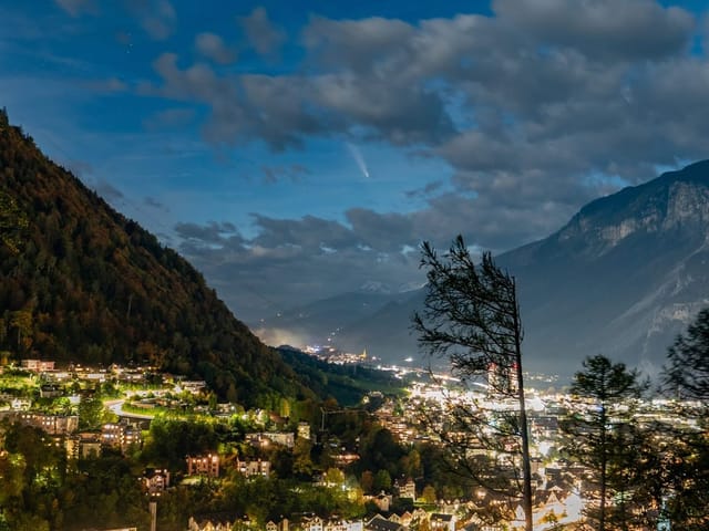 Nächtliche Stadtlandschaft mit Bergen und beleuchteten Häusern.