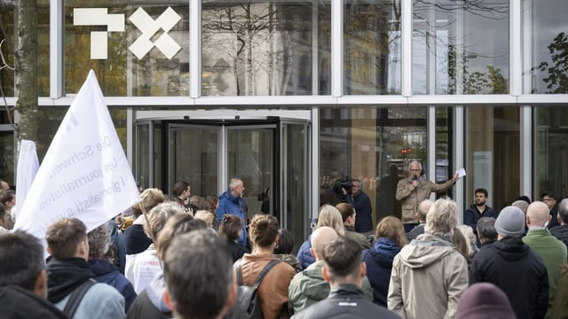 Protestierende schauen Richtung Eingang des Hauptgebäudes und hören einem Redner zu.