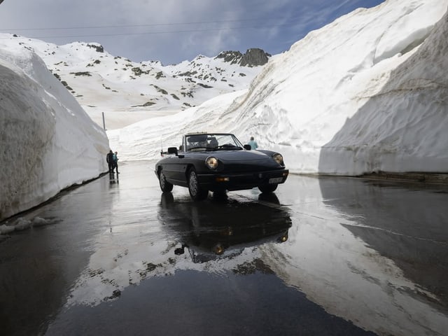 Cabrio fährt auf Strasse. An den Seiten hohe Schneemauern.