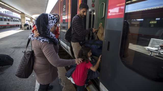 Eine Frau und ein Mann mit zwei Kindern besteigen einen Zug in Wien 