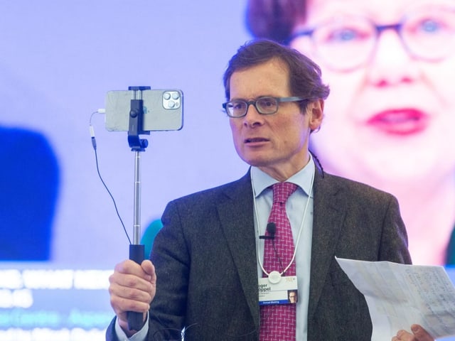 Mann mit einem Selfie-Stick in der Hand blickt in ein Smartphone.